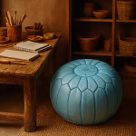 A Moroccan leather pouf blue in a rustic artisan studio with wooden tools, pottery, and sketchbooks.