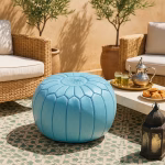 A Moroccan leather pouf blue on a tiled patio, surrounded by rattan chairs and traditional tea setup.