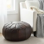 Multi-toned Chocolate Brown Ottoman on a light rug next to a white armchair and a chunky grey knit throw blanket.