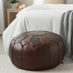 Chocolate Brown Ottoman placed at the foot of a bed with white bedding, a grey blanket, and natural wood side table.