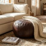 A warm living room interior featuring a leather Chocolate Brown Ottoman placed on a vintage rug next to a cream-colored sofa with a knit throw.