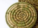 Close-up of artisan hand-woven straw kitchenware placemat showing natural palm fiber spiral pattern and craftsmanship