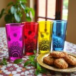 Rainbow henna tea cups on a patterned tablecloth showing black hand-painted henna motifs and vibrant hues