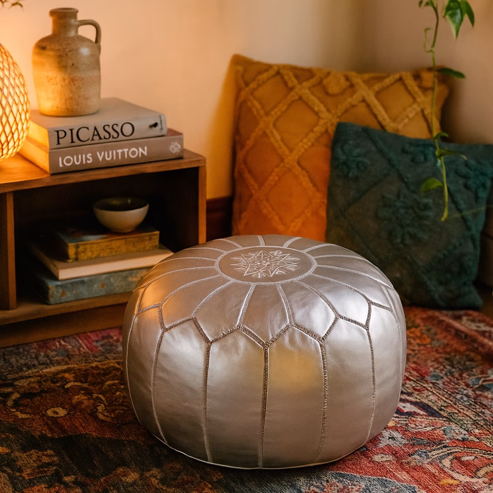Cozy reading nook featuring a leather Pouf Silver on a patterned rug, surrounded by cushions and books.