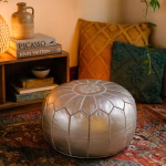 Cozy reading nook featuring a leather Pouf Silver on a patterned rug, surrounded by cushions and books.