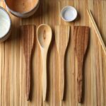 Four piece lemon wood kitchenware 12" utensil set arranged on bamboo mat with Asian cuisine bowls