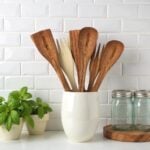 Lemon wood kitchenware 12" spoons and spatulas displayed in white vase with basil plant on kitchen counter