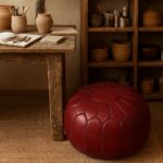 Handstitched leather floor ottoman in deep red, round Moroccan pouf beside rustic wood table