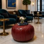 Round leather floor ottoman in deep red, elegant Moroccan pouf in luxury lobby with velvet chairs