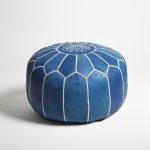 Studio photograph of a cobalt blue leather floor ottoman with white embroidery on a neutral white background.