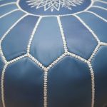 Macro close-up of the white hand-stitching and embroidery on the vibrant blue leather floor ottoman.