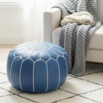 Vibrant blue leather floor ottoman on a wooden floor near a white couch and a small potted houseplant.