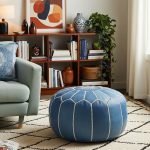 Blue leather floor ottoman in an eclectic living room with a mint green chair, patterned rug, and warm wood bookshelf.