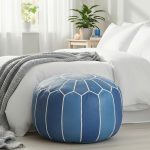 Blue leather floor ottoman at the foot of a bed with white bedding, a grey throw, and natural lighting.