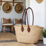 Straw tote bag with long leather handles on wooden bench - French market basket in farmhouse entryway