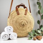 Round straw bag on park bench with fruit, woven circular tote perfect for picnic and farmers market shopping