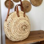 Handwoven round straw bag with leather handles displayed on shelf, natural fiber basket tote with embroidered details