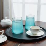 Group of blue and green handblown wine glasses on an outdoor wooden table in sunlight