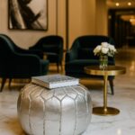 Silver leather round ottoman with book in elegant living room - luxe metallic pouf footrest accent