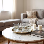 Gold tray of moroccan tea glasses on a round marble coffee table in a cozy neutral-toned living room.