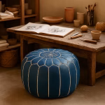 Handcrafted leather pouf blue in a rustic studio setting, surrounded by sketchbooks and pottery tools