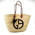 Designer straw tote bag with black logo and brown leather handles on white background