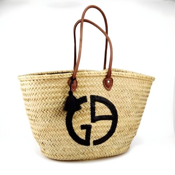 Designer straw tote bag with black logo and brown leather handles on white background