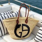 Close-up of handwoven designer straw tote bag with black logo on boat cushions
