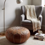Natural tan leather pouf next to reading chair with throw blanket