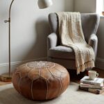 Leather floor ottoman styled with gray armchair and throw blanket in modern living room setting