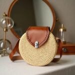 Round straw crossbody bag with cognac leather flap and silver clasp in home interior