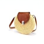 Round straw crossbody bag with brown leather flap and silver clasp on white background