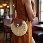 Woman wearing round straw crossbody bag with leather flap and brown dress in elegant setting
