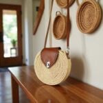 Round straw crossbody bag hanging on wood console with woven baskets and mirror decor