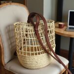 Straw backpack with open lattice weave and herringbone base on upholstered chair beside straw hat