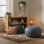 Gray leather round ottoman Moroccan pouf styled in bohemian living room with colorful rug and plants