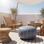 Gray leather round ottoman floor pouf on Moroccan terrace with traditional lanterns and wicker furniture