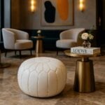 Luxury white leather round ottoman pouf in sophisticated hotel lobby with gold accent table and modern chairs