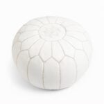 White leather round ottoman with hand-embroidered star design and geometric stitching on white background