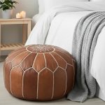 Multi-toned brown Leather Round Ottoman with white stitching at the foot of a bed with crisp white bedding and a grey knit throw.