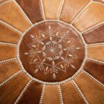 Close-up detail of the intricate hand-stitched white embroidery on the top mandala of a Moroccan Leather Round Ottoman.