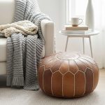 Leather Round Ottoman next to a white armchair draped with a grey and cream chunky knit throw.