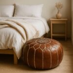 Genuine leather floor ottoman pouf beside bedroom with minimalist natural beige linens and wood furniture