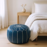 Minimalist bedroom scene featuring a leather pouf blue next to a light wood nightstand and white bedding.