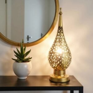 Decorative brass bedside lamp lit on shelf with succulent and mirror, casting warm ambient glow