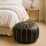 Round black leather floor ottoman pouf with white contrast stitching beside bed in minimalist bedroom