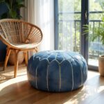 Blue leather floor ottoman with white embroidered star pattern on wooden floor near rattan chair in bright sunlit room
