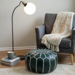 Green leather floor ottoman with white star embroidery beside gray chair, cozy throw blanket, and floor lamp in modern living room