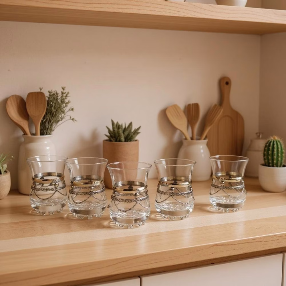 Row of five silver-trimmed moroccan tea glasses arranged on a wooden kitchen counter with potted succulents.
