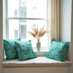 Teal floral pillow covers displayed on windowsill with vase and natural lighting